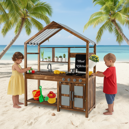 Children playing with a wooden play kitchen on a sandy beach with palm trees and ocean in the background.