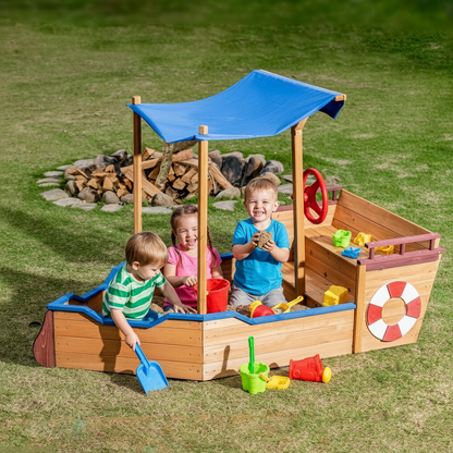 Children playing in a wooden pirate ship sandbox with a blue canopy on a grassy area.