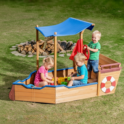 Children playing in a wooden pirate ship sandbox with a blue canopy on a grassy area.
