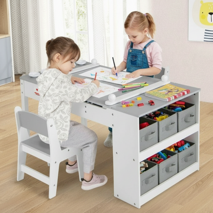 Two children sitting at a white and gray art table with storage bins, drawing and playing.
