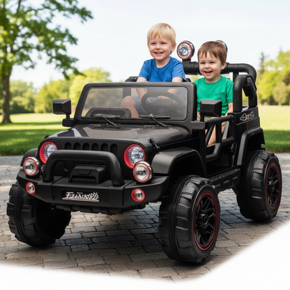 Two children sitting in a black toy jeep on a paved area with greenery in the background.